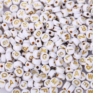 Macro shot of white acrylic alphabet beads with gold letters for DIY jewelry making