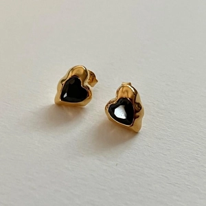 Detail of gold lava heart earrings with black gems and butterfly backings on paper