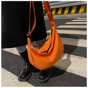 On-street shot of vibrant orange nylon crescent crossbody bag worn over dark clothing