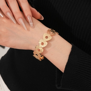 Close-up of a gold metal hollow heart bracelet with engraved patterns on model's wrist