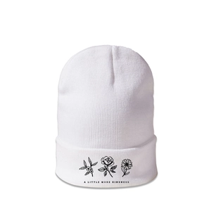 Close-up of white knitted beanie featuring three flower illustrations and kindness slogan