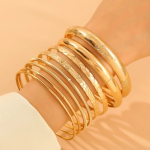 Detail of stacked bohemian gold alloy bracelets featuring smooth and textured finishes