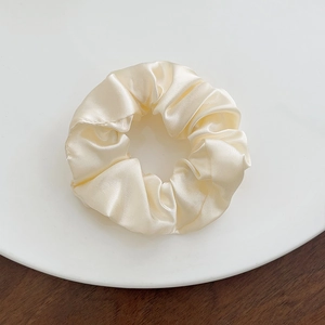 Close-up of a cream white silk scrunchie with soft satin luster on a ceramic plate