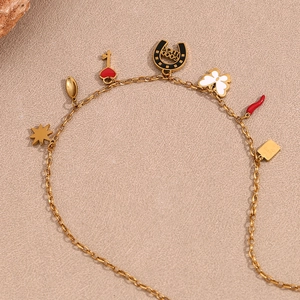 Primer plano detallado del collar chapado en oro de 18K con varios dijes sobre fondo beige