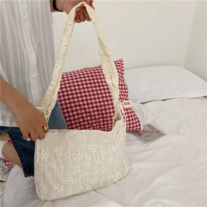 Detail of floral daisy print tote bag with ruffled strap held against white bedding