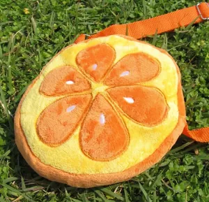 Detail of plush orange slice crossbody bag with adjustable strap on grass background
