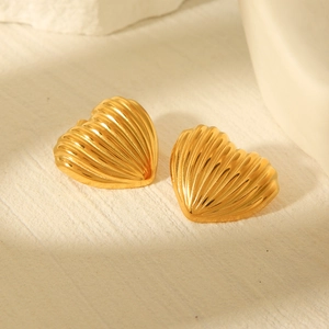 Close-up of heart-shaped gold earrings with vertical striped texture on stone surface