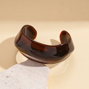 Macro detail of the amber-textured wide acrylic bangle with polished finish and open design
