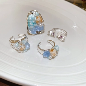 Detailed macro of a silver open ring with shells and blue beads on a white tray