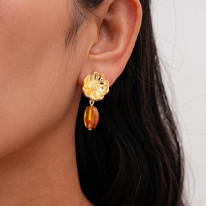 Macro detail of amber resin drop earrings with gold floral studs on model ear