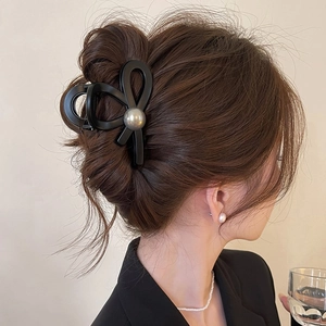 Side view of a black matte bow hair claw clip with large pearl on model's hair