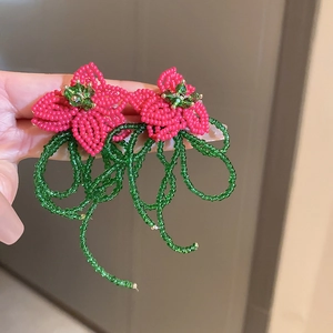 Macro shot of handmade red floral beaded earrings with green rhinestone centers and fringes