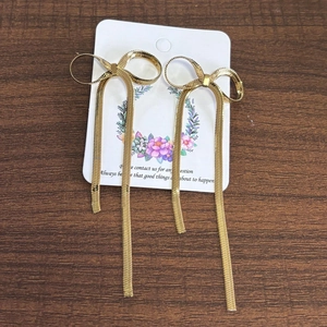 Detailed view of long gold bow tassel earrings with snake chain on wooden background
