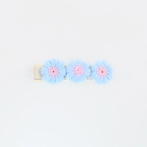 Detail of three light blue hand-knitted crochet flowers with pink centers on a hair clip