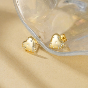 Detailed view of heart-shaped gold stud earrings featuring micro-pave white zircon stones