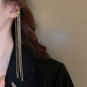 Close-up of elegant gold long tassel chain ear cuff on model wearing a black blazer