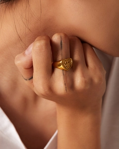 Close-up of a gold-plated heart-shaped signet ring with an embossed angel on the finger