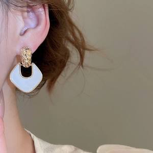 Close-up of model wearing gold and white enamel geometric U-shaped earrings