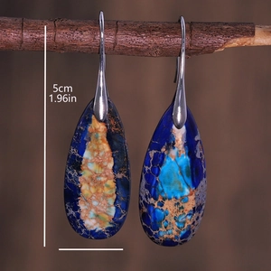 Detailed view of blue emperor stone teardrop earrings hanging on a vintage wooden branch