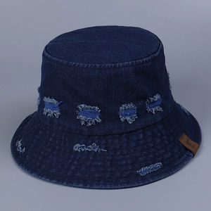 Detailed view of dark blue denim bucket hat with distressed holes and leather brand patch