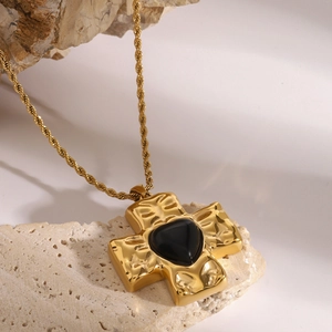 Detailed shot of a gold twist chain necklace featuring a textured cross and black heart stone