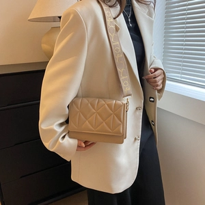Macro view of beige quilted PU leather handbag with decorative wide shoulder strap