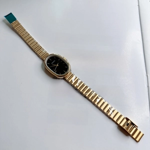 Close-up of elegant small oval quartz watch with gold link strap on a magazine