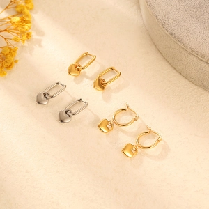 Polished heart pendant hoop earrings in gold and silver finish on stone surface