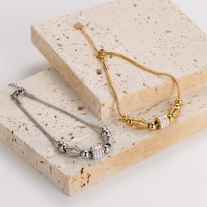Gold and silver snake chain bracelets with sparkling zircon charms on stone display