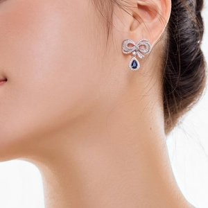 Detail of silver bow earrings with blue teardrop gemstone on female model ear
