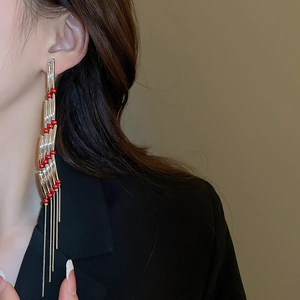 Close-up of elegant long rectangular tassel earrings with gold finish and red beads