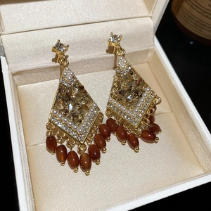 Macro detail of diamond-encrusted diamond-shaped crystal tassel earrings in brown finish