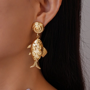 Close-up of a gold-toned fish-shaped metal earring worn by a model with dark hair