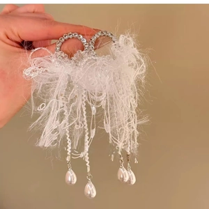 Detail view of white feather fringe earrings with silver rhinestones and pearl drops