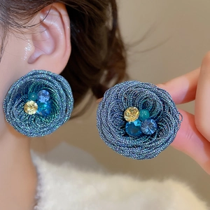 Detailed view of woven teal flower earrings with yellow and blue bead centers