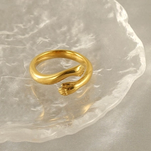 Polished 18k gold plated stainless steel hugging hands ring on textured glass base