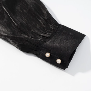 Détail du poignet noir élégant avec tissu texturé et boutons de perles à bordure dorée