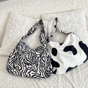 Flat lay of large corduroy crossbody bags in zebra and cow patterns on white plush rug
