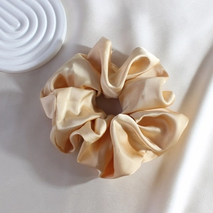 Detailed view of a gold satin silk scrunchie with soft texture on a silk background