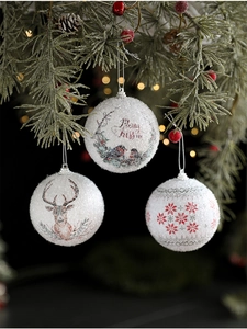 Close-up of white foam Christmas balls with reindeer and bird patterns hanging on a tree