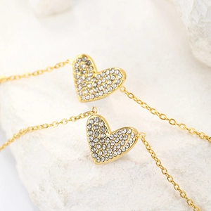 Close-up of gold-plated heart pendants with micro-paved sparkling crystals on a stone background