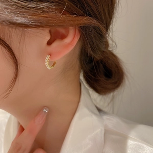 Close-up of a gold minimalist hoop earring with paved zircon stones on a female model