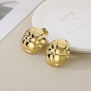 Close-up of golden croissant style stud earrings with quilted texture on white porcelain