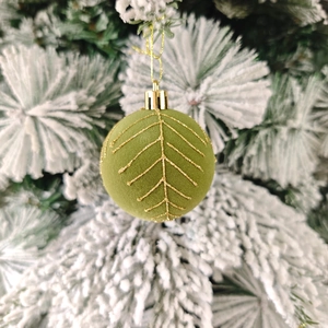 Gros plan d'une boule de Noël en velours vert avec motifs dorés sur branche enneigée