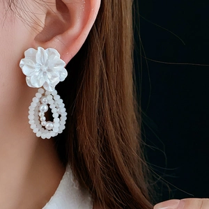 Close-up of floral pearl earrings with shell petals and beaded charms on model