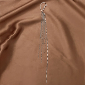 Detailed macro view of silver tassel ear cuff with rhinestones and faux pearls on silk fabric