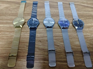 Row of quartz watches with metal mesh straps in gold, silver, black, and blue colors