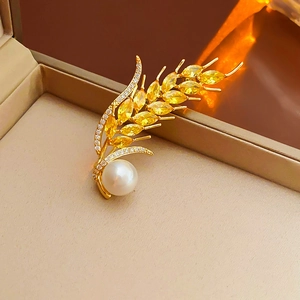 Macro detail of wheat ear brooch with yellow gems and a round white pearl on a jewelry box