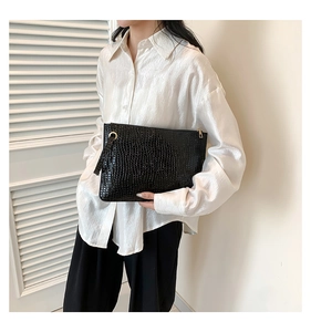 Close-up of black crocodile pattern envelope clutch with gold zipper and metal ring