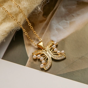 Collana con ciondolo a farfalla dorata con zircone e perla su sfondo in tessuto